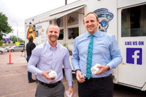 Two young men holding burritos in front of a food truck.